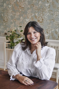 Porträttbild på Sveriges Mästerkock Tess Medina klädd i vitt vid ett bord.